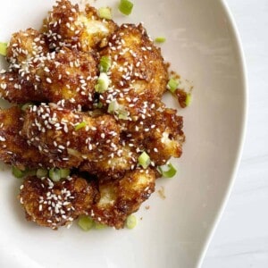 honey garlic whole baked cauliflower topped with scallions and sesame seeds.