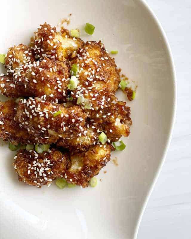 honey garlic whole baked cauliflower topped with scallions and sesame seeds.