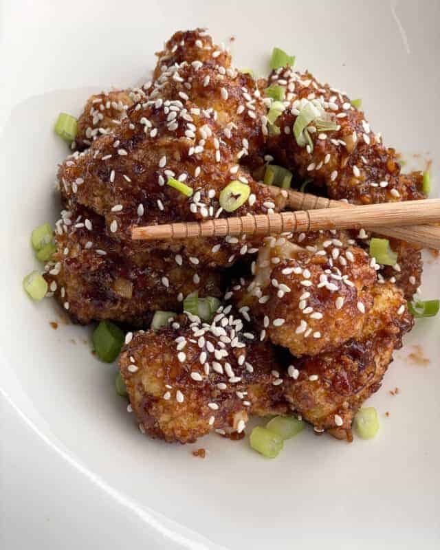 a bowl of honey garlic baked cauliflower with chopsticks grabbing a piece.