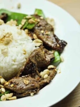 A plate of beef with snow peas surrounding a mound of white rice.