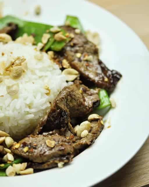 A plate of beef with snow peas surrounding a mound of white rice.