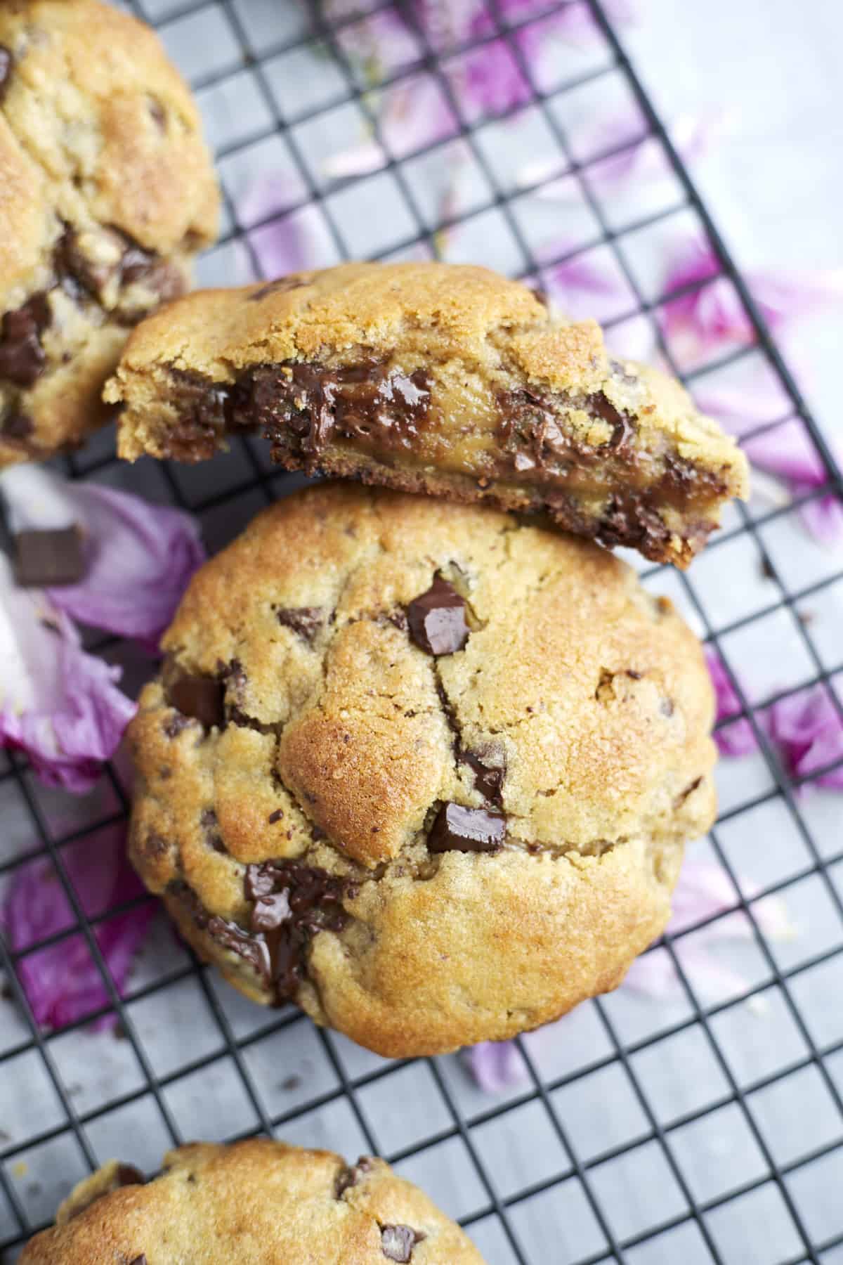 ultimate chocolate chip cookies in a cooling rack. One large cookie cut in half showing the inside.