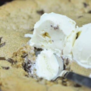 Peanut Butter Choc Chip Skillet Cookie Recipe topped with vanilla ice cream being scooped with a spoon