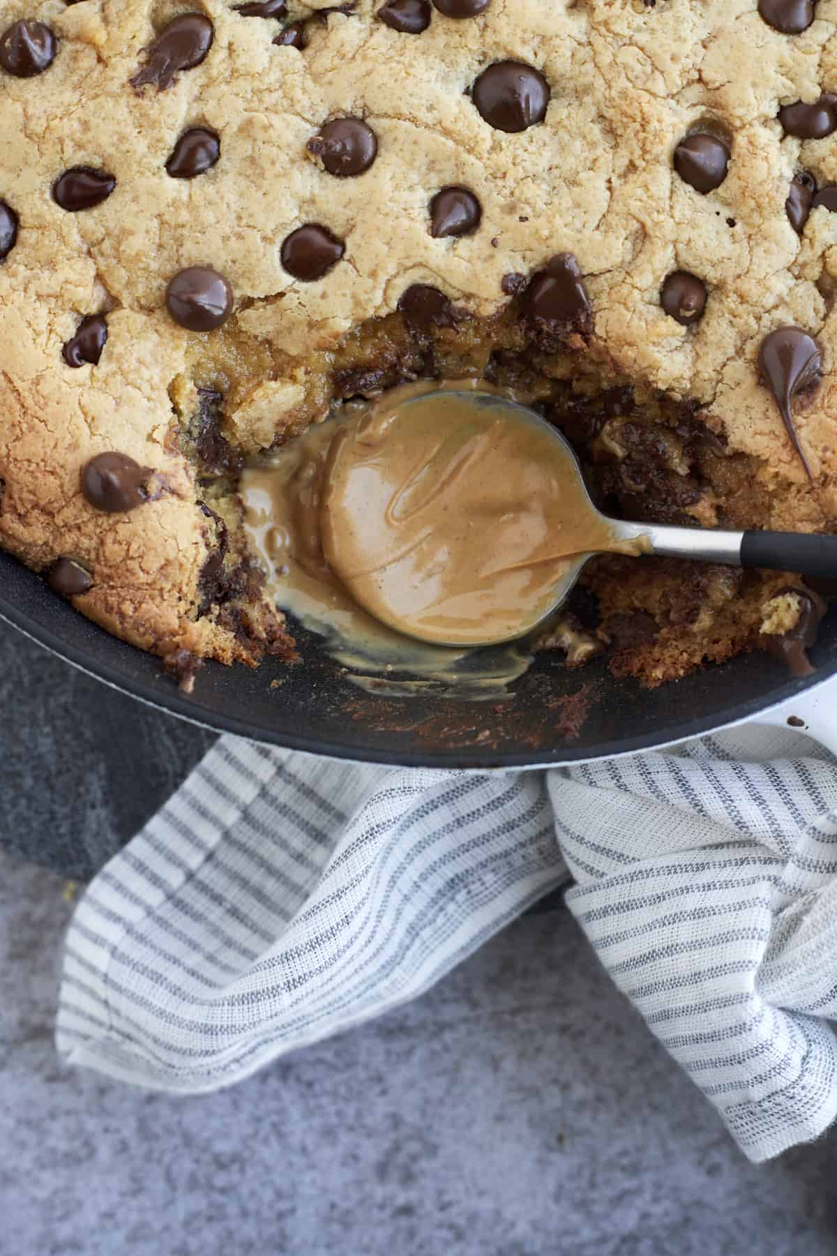 close up image of a peanut butter coated spoon in a peanut butter chocolate chip cookie skillet