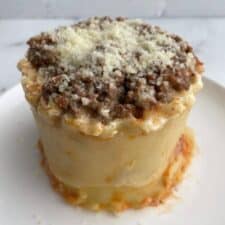 Lasagna in a mug on a plate topped with Parmesan cheese.