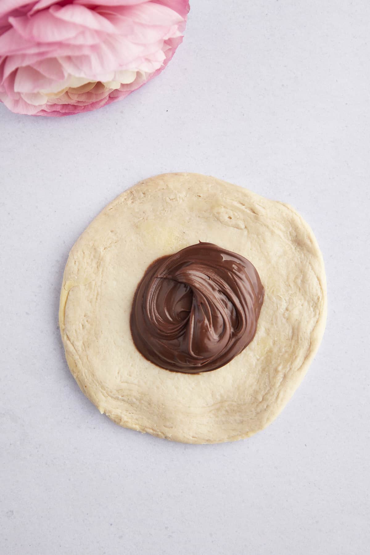 Raw biscuit dough flattened into a circle with a dollop of Nutella in the center. 
