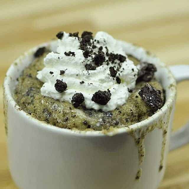 Cookies and cream mug cake topped with whipped cream and Oreo pieces.