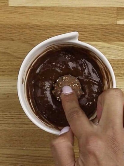 a finger pressing a Ferrero Rocher candy into mug cake batter