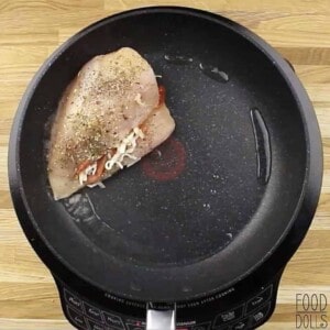Raw cheesy pizza stuffed chicken breast in a skillet.