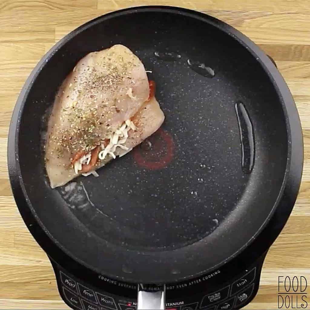 Raw cheesy pizza stuffed chicken breast in a skillet.