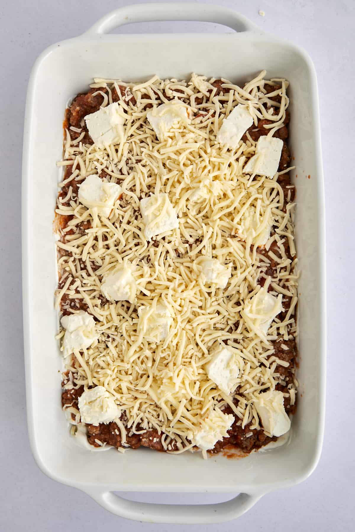 unbaked million dollar spaghetti topped with chunks of cheese and shredded mozzarella 