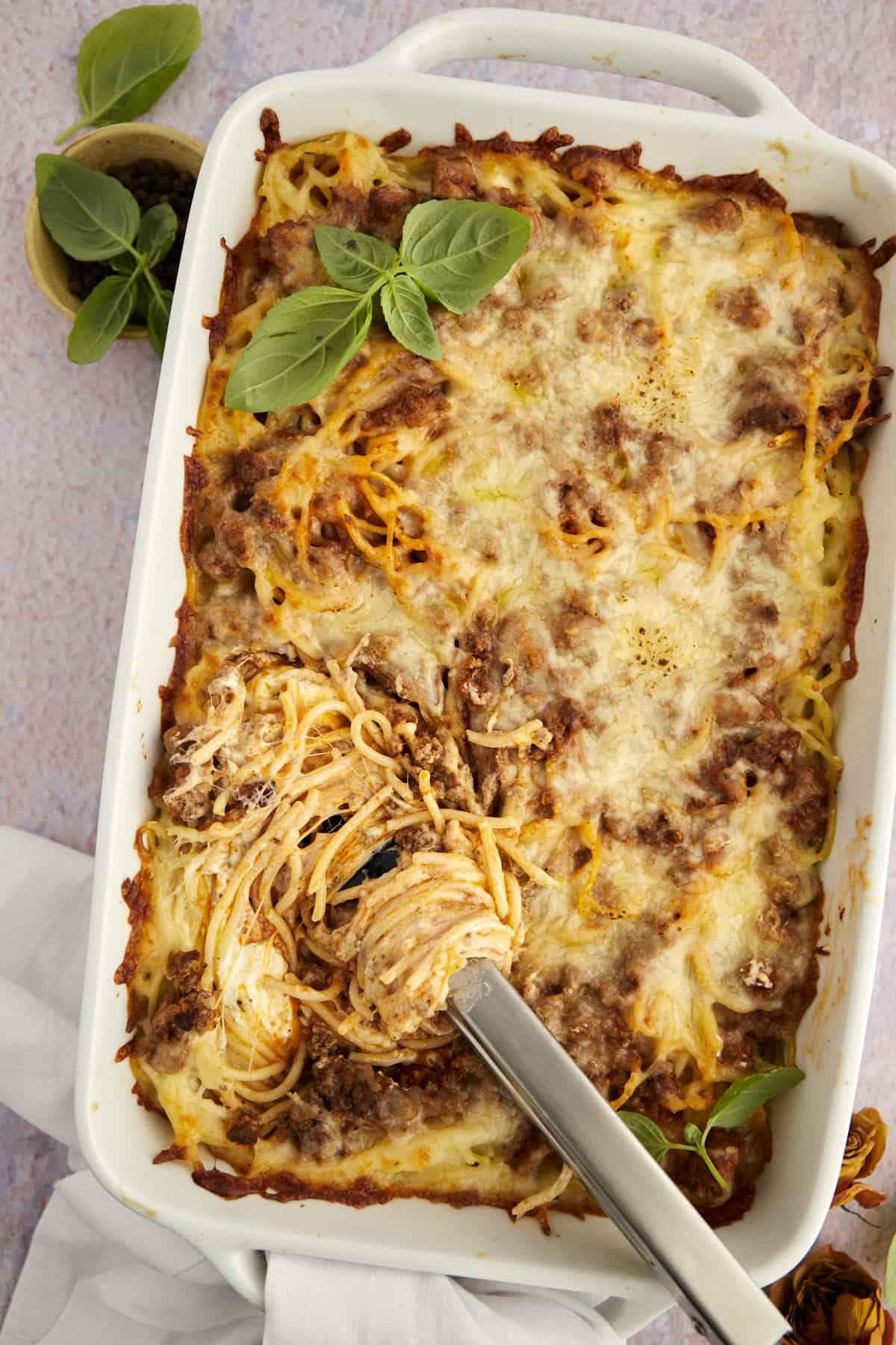 tongs twirling a serving of baked million dollar spaghetti casserole in a dish.