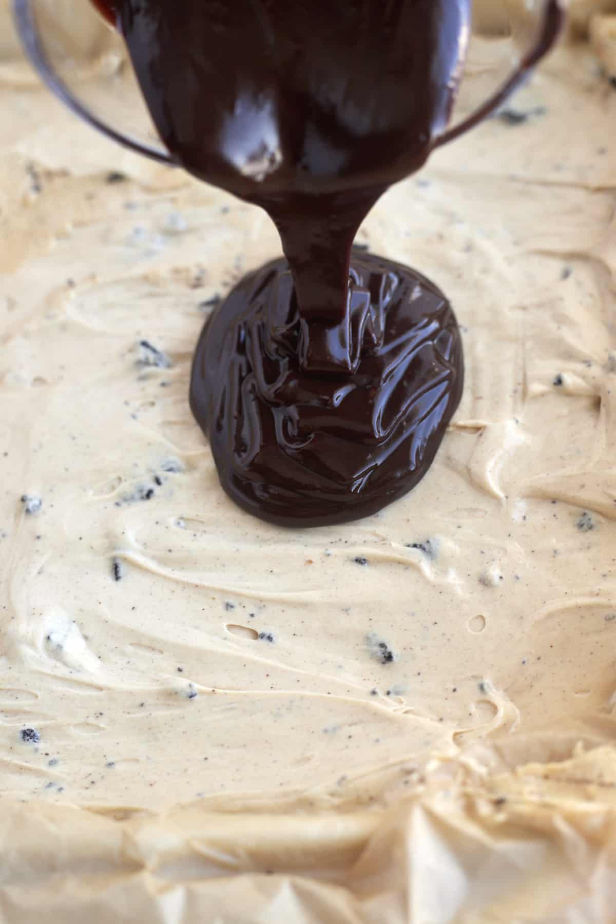 chocolate ganache being poured over a cream cheese peanut butter filling