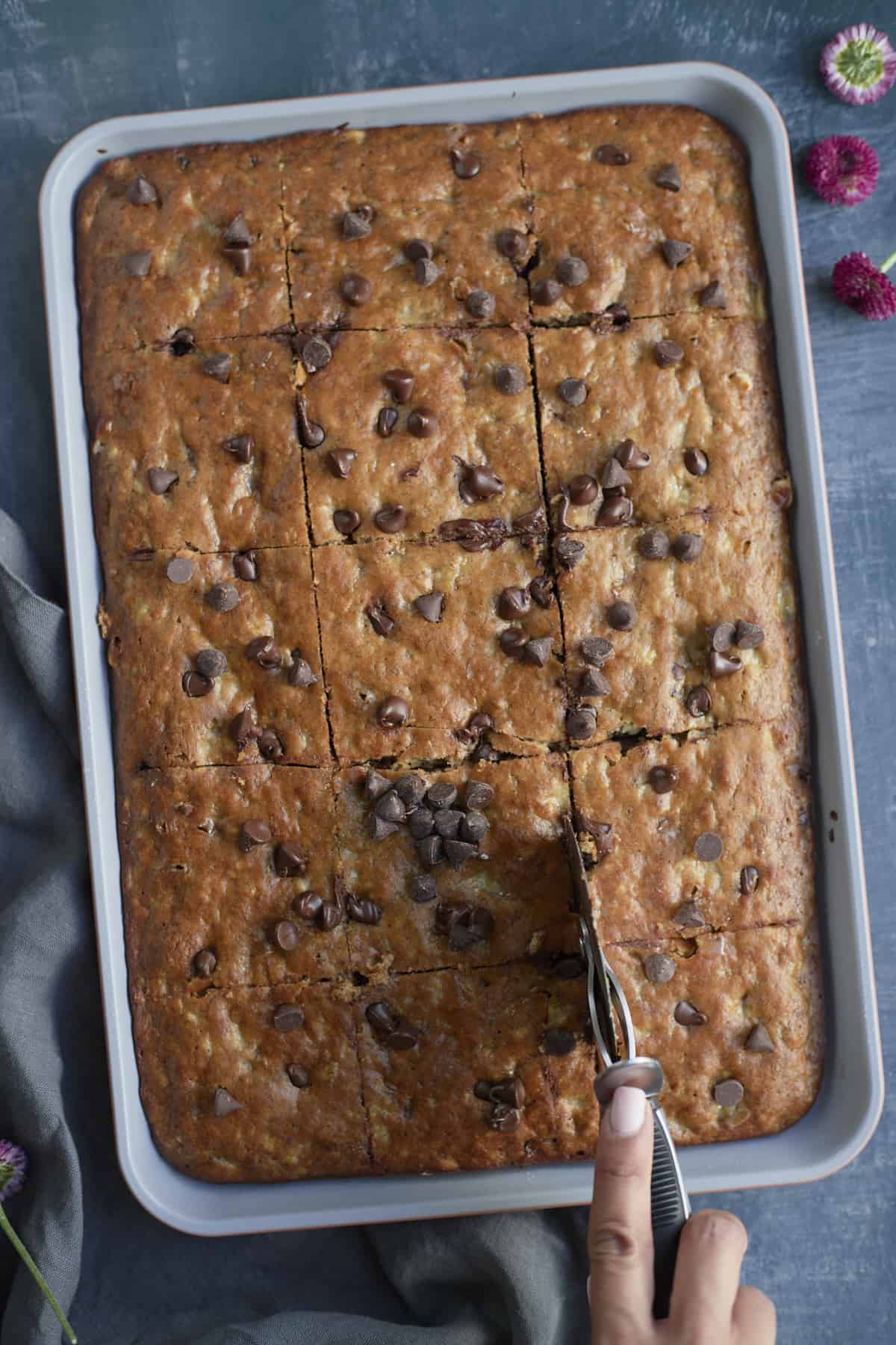 banana bread in a sheet pan. A pizza cutter cuts it into slices
