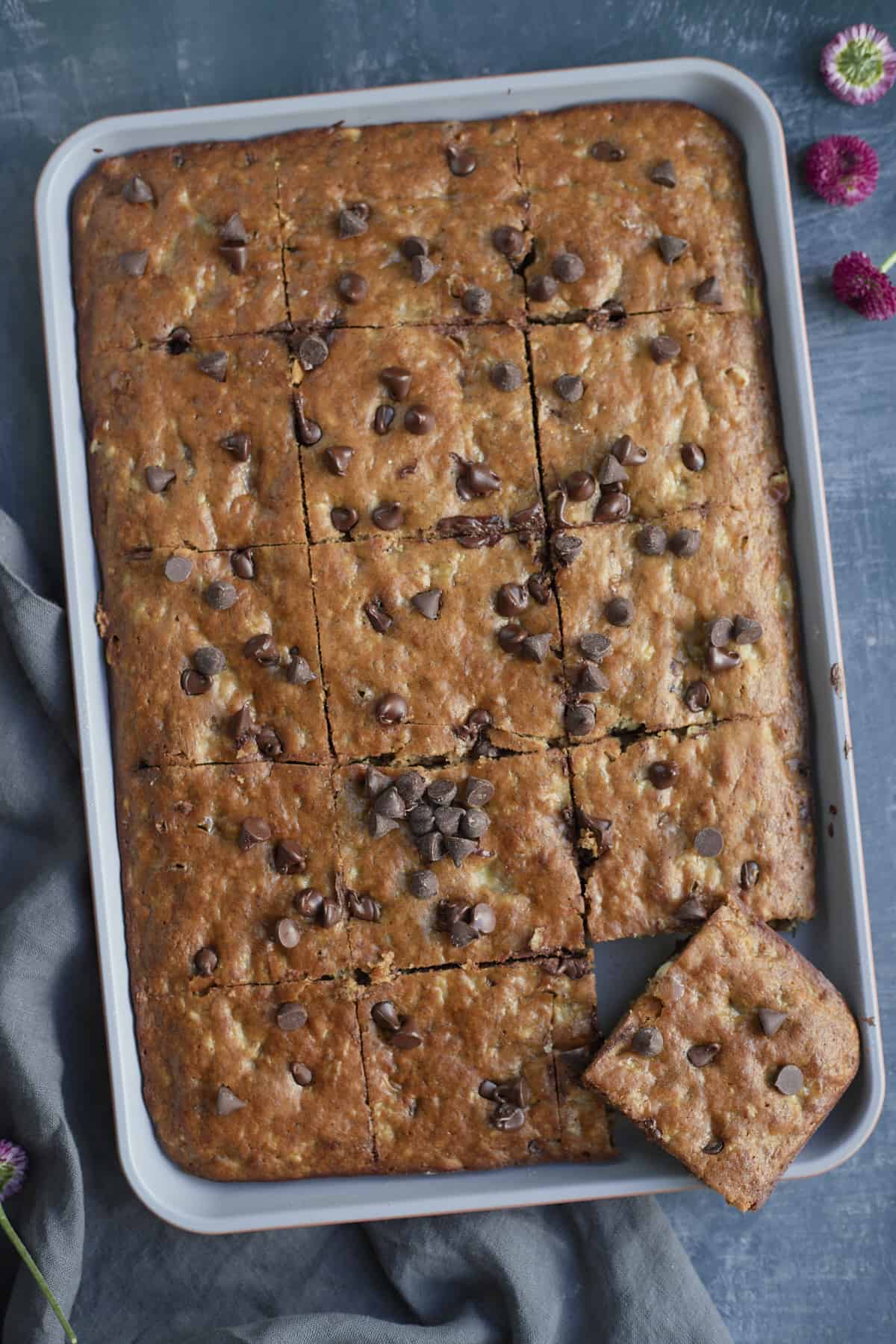 overhead of a banana bread cut into squares on a sheet pan with one off of the pan.
