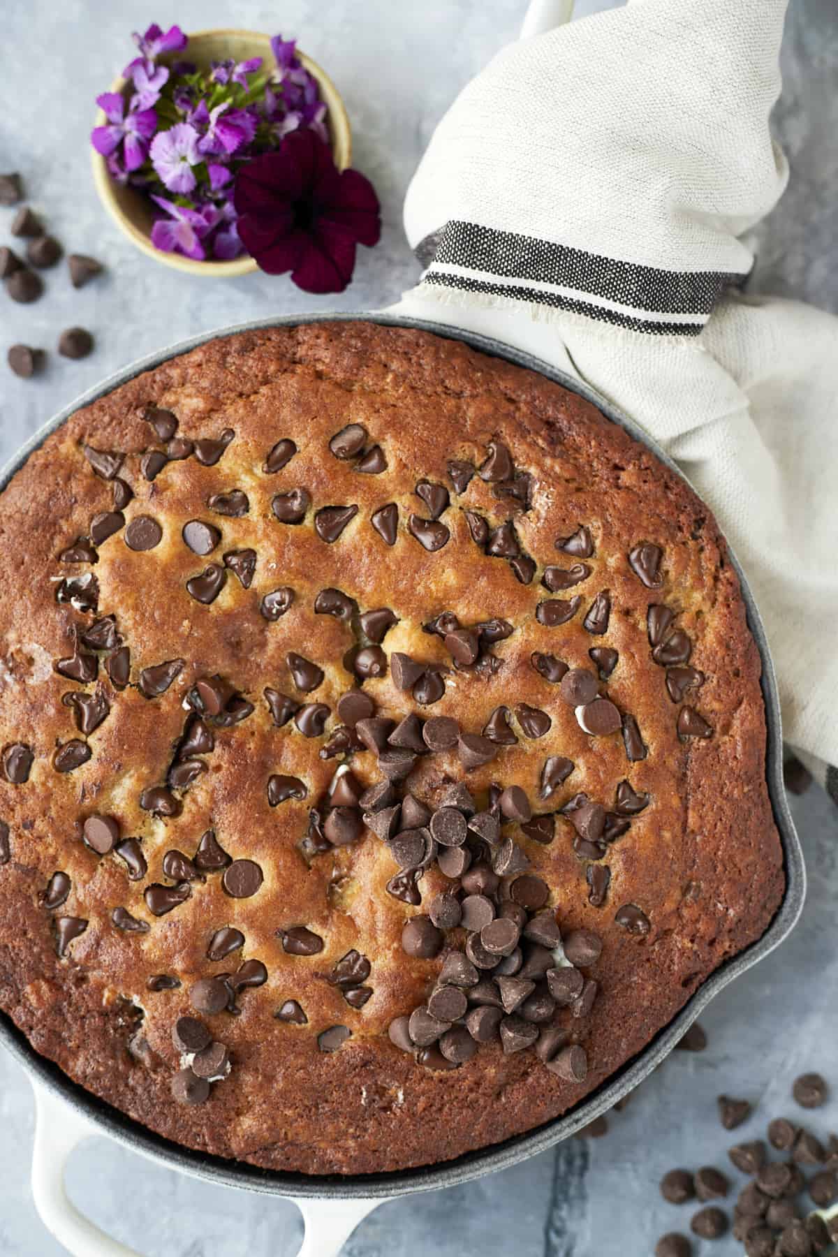 overhead of the skillet banana bread with chocolate chips on top and dressed up with a towel and flowers