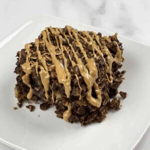 A serving of chocolate peanut butter oatmeal bake on a plate topped with a drizzle of peanut butter.