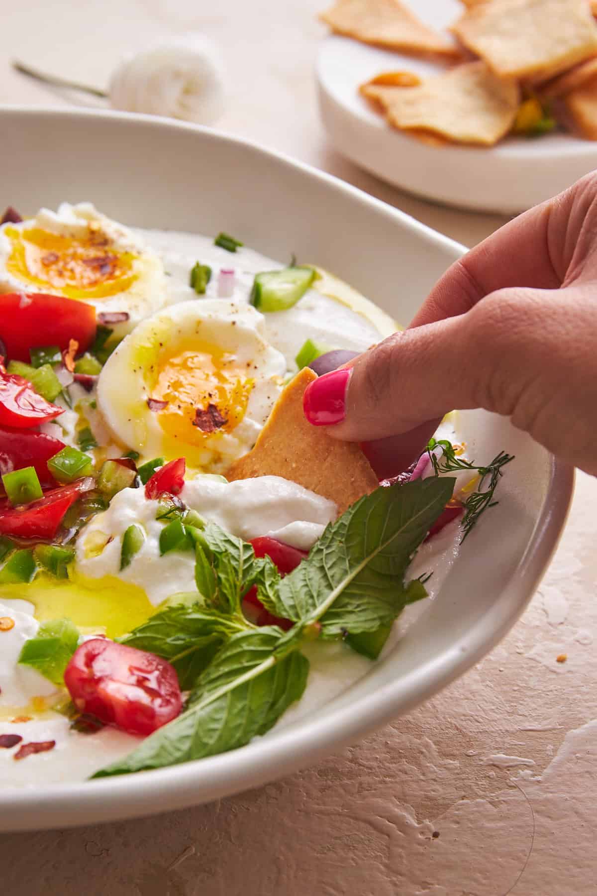 A hand dipping a pita chip into a bowl of whipped cottage cheese salad. 
