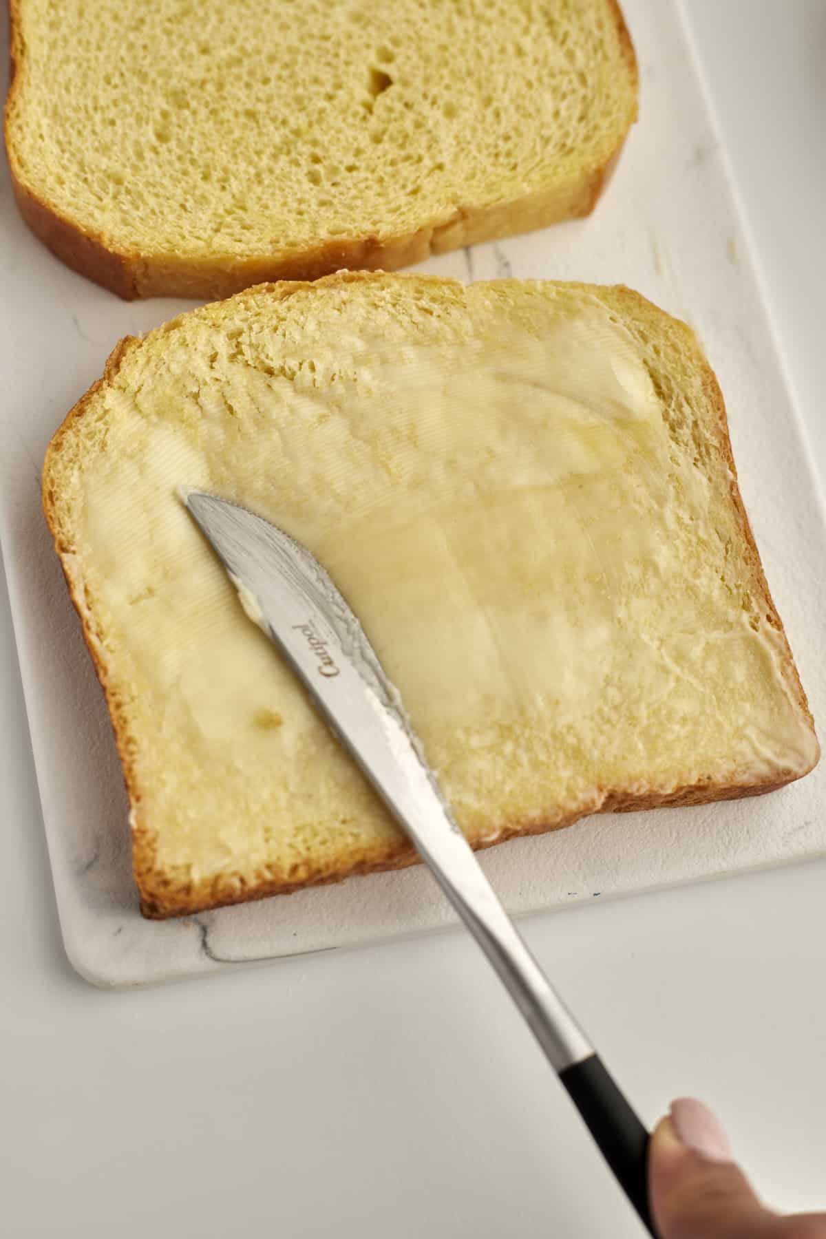 two pieces of bread with a hand buttering one