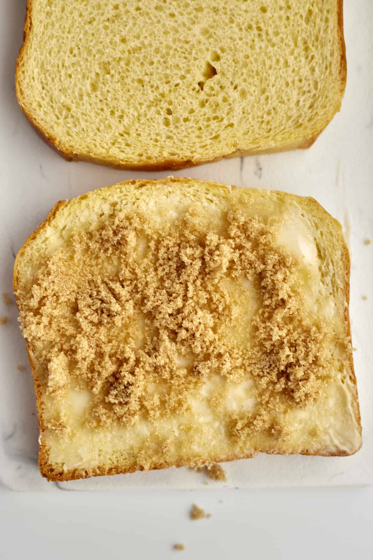 two slices of brioche bread, one buttered and topped with brown sugar