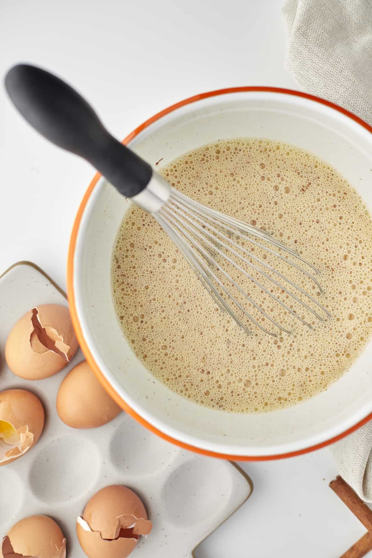 an overhead image of a bowl of an egg mixture with eggs on the side to make a baked cinnamon french toast recipe