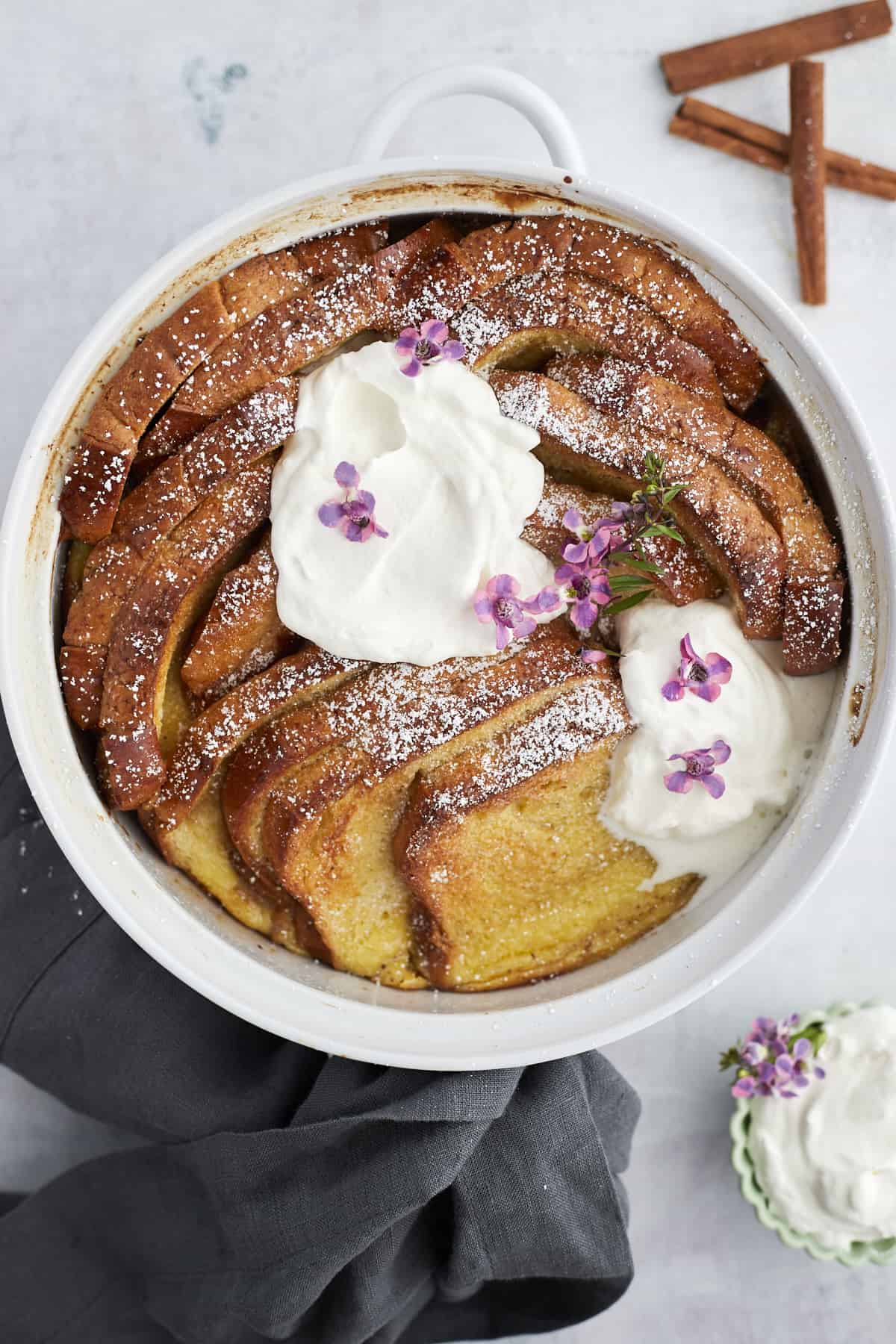 a white baking dish with baked cinnamon french toast topped with powdered sugar and marscapone cheese