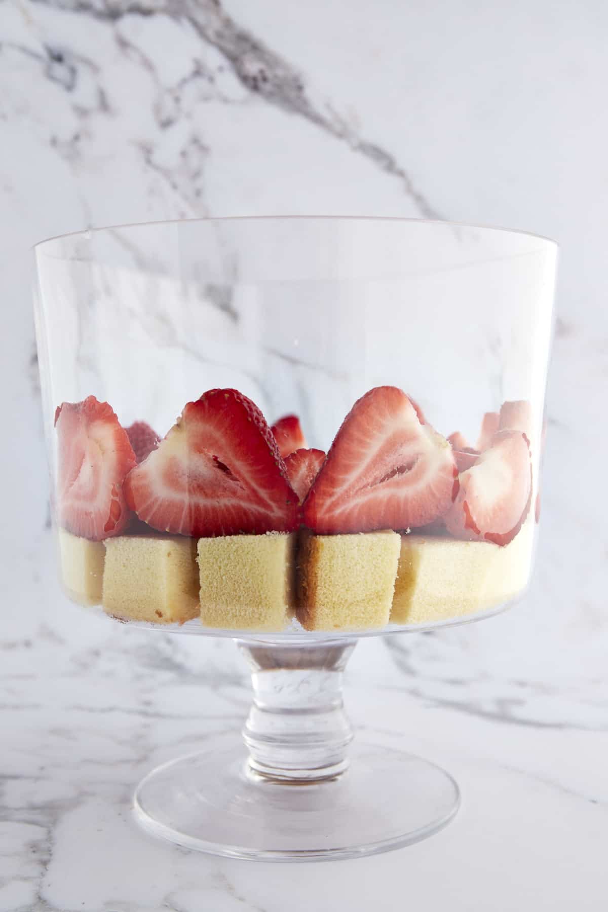 A trifle bowl with a layer of pound cake cubes topped with strawberries. 