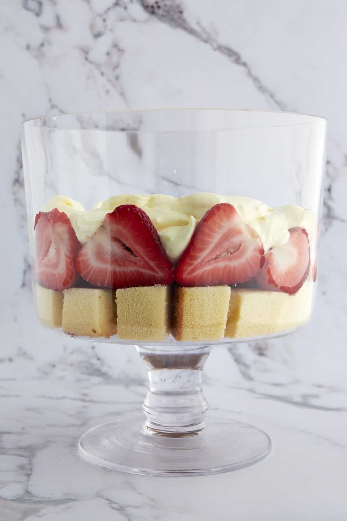 A trifle bowl with a layer of pound cake, strawberries, and whipped topping. 