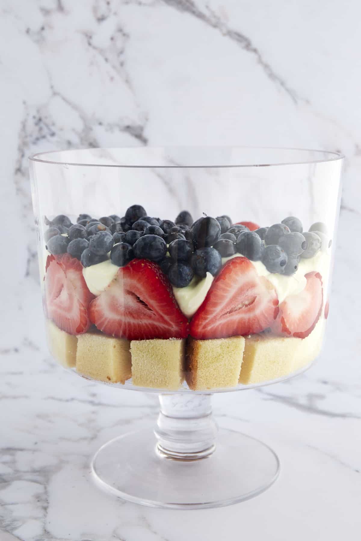 A trifle bowl with a layer of pound cake, strawberries, whipped topping, and blueberries. 