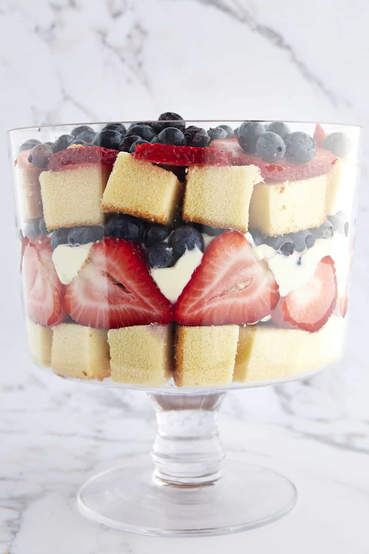 A trifle bowl full of layers of pound cake, strawberries, whipped topping, and blueberries. 