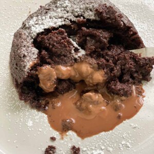 a hazelnut chocolate mug cake on a white plate that has been broken into and is oozing chocolate
