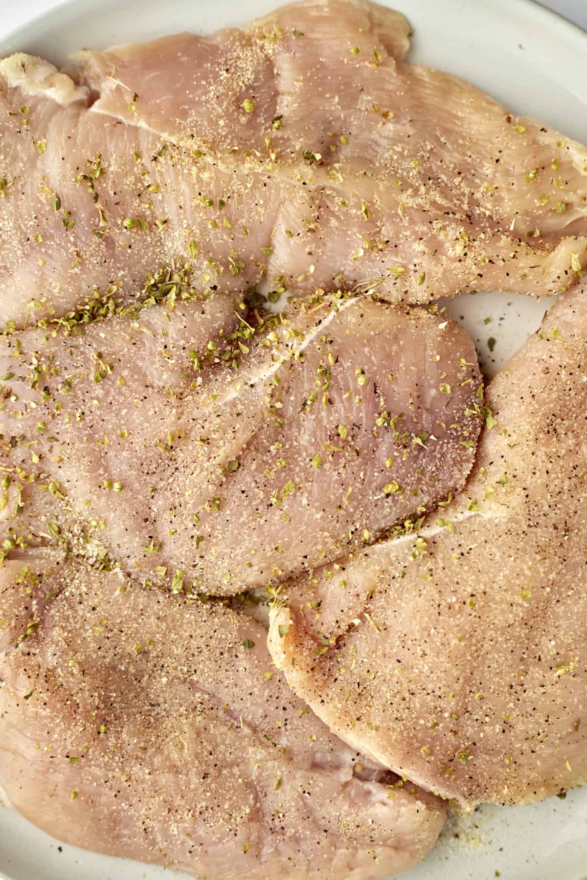 Raw seasoned chicken breasts on a white plate. 