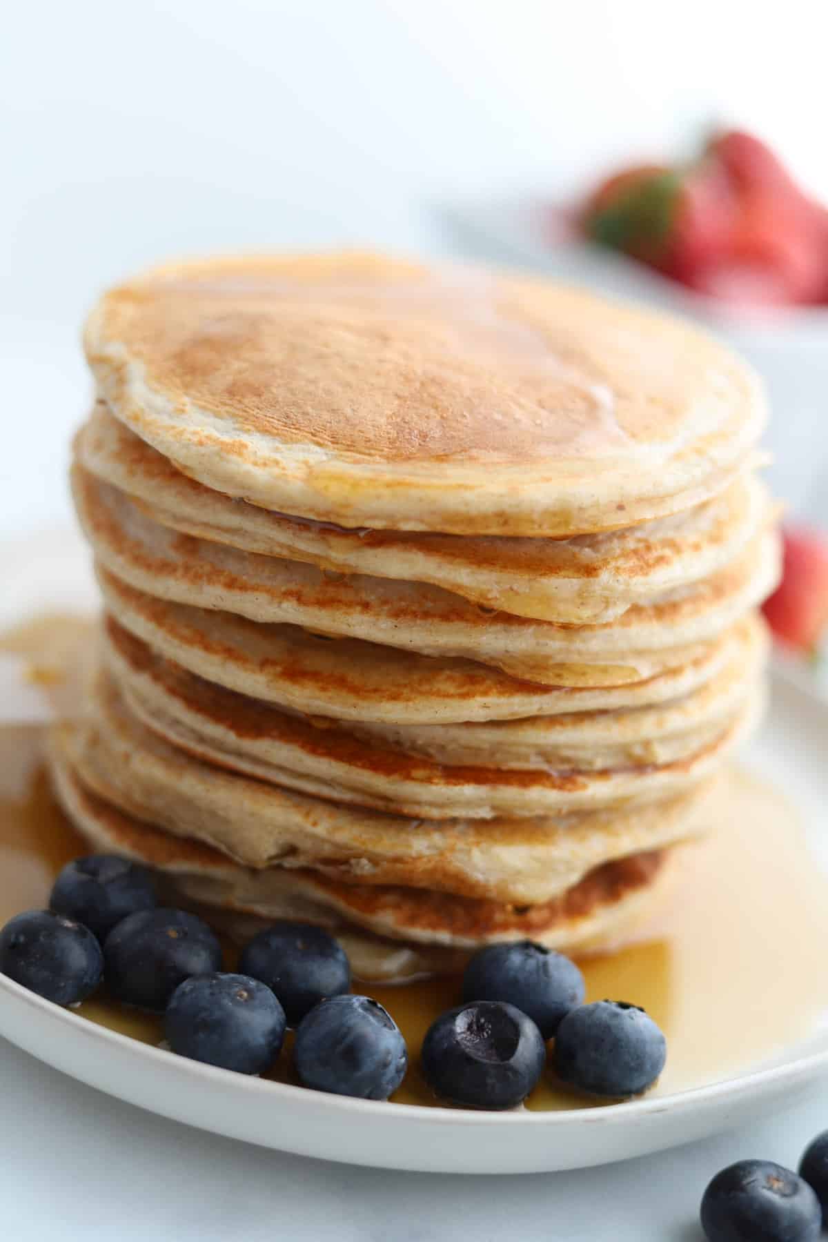 a stack full of cottage cheese protein pancakes on a plate topped with syrup with blueberries on the side.