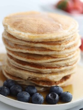 a stack of cottage cheese protein pancakes on a plate topped with syrup with blueberries on the side