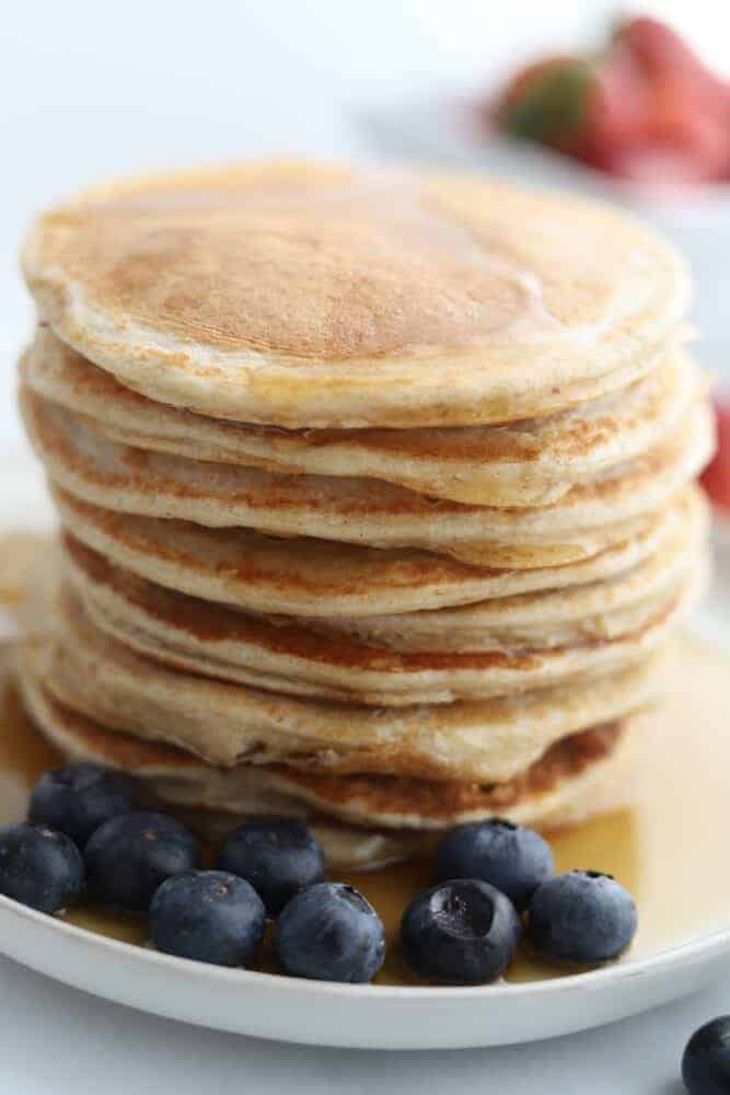 a stack of cottage cheese protein pancakes on a plate topped with syrup with blueberries on the side