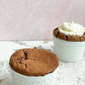 two ramekins full of chocolate soufflé with one topped with whipped cream