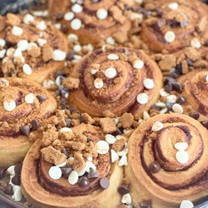 Biscoff cinnamon rolls in a skillet topped with semi-sweet chocolate chips, white chocolate chips, and Biscoff cookies.