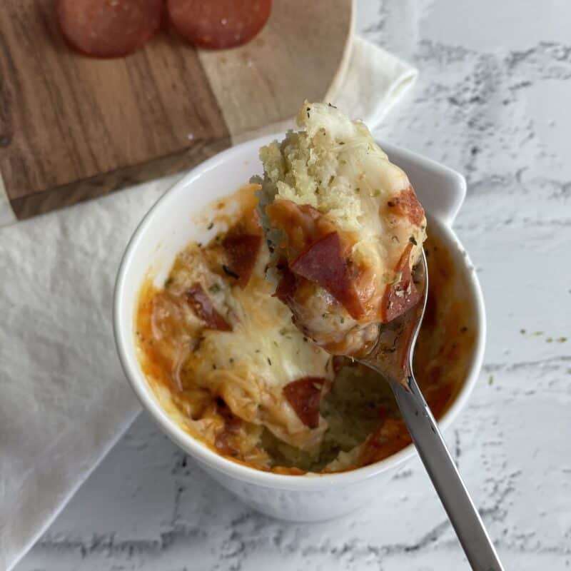 A spoon lifting a bite of pizza in a mug. 