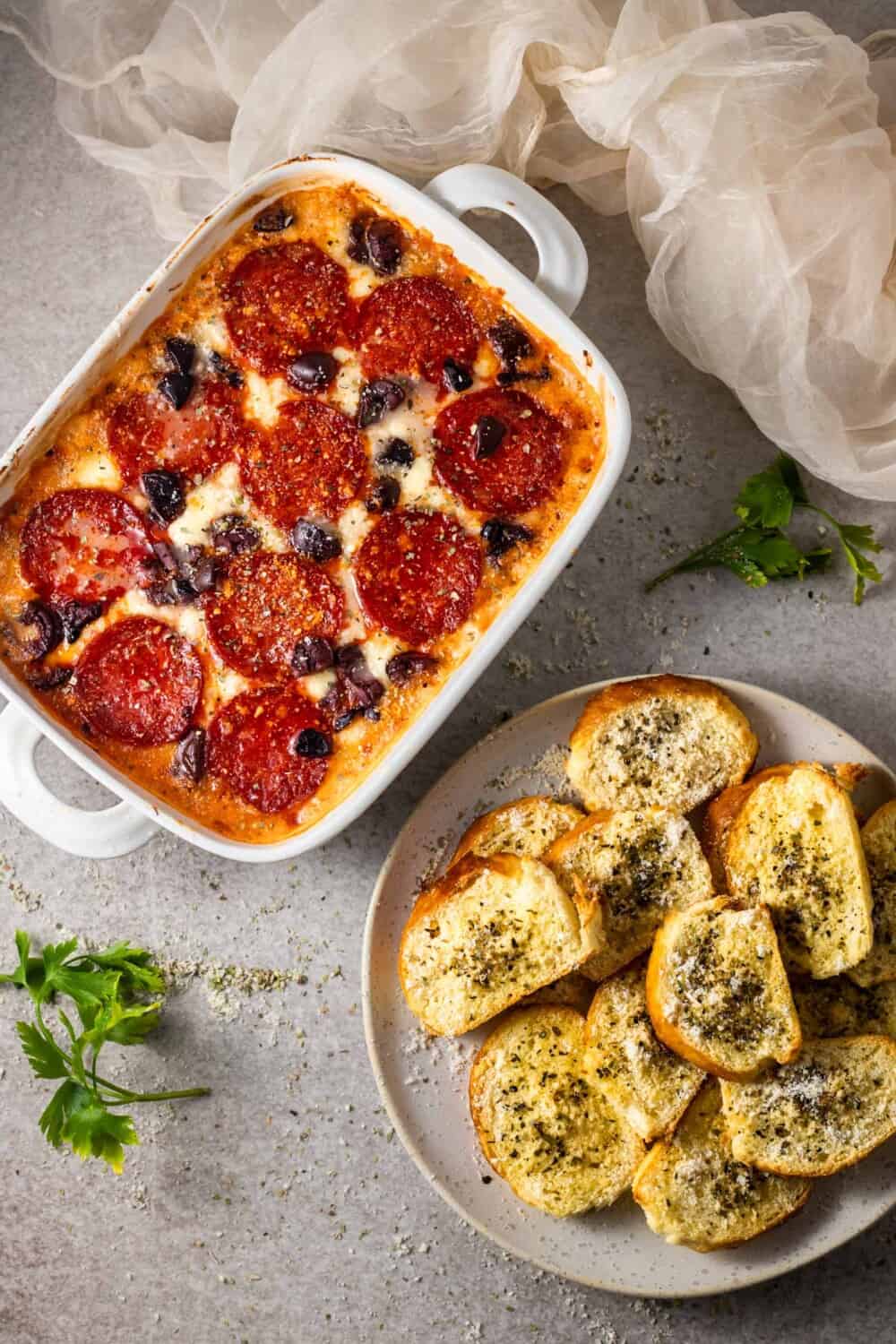 a baking dish full of pizza dip and a plate of baked cheese crostini.