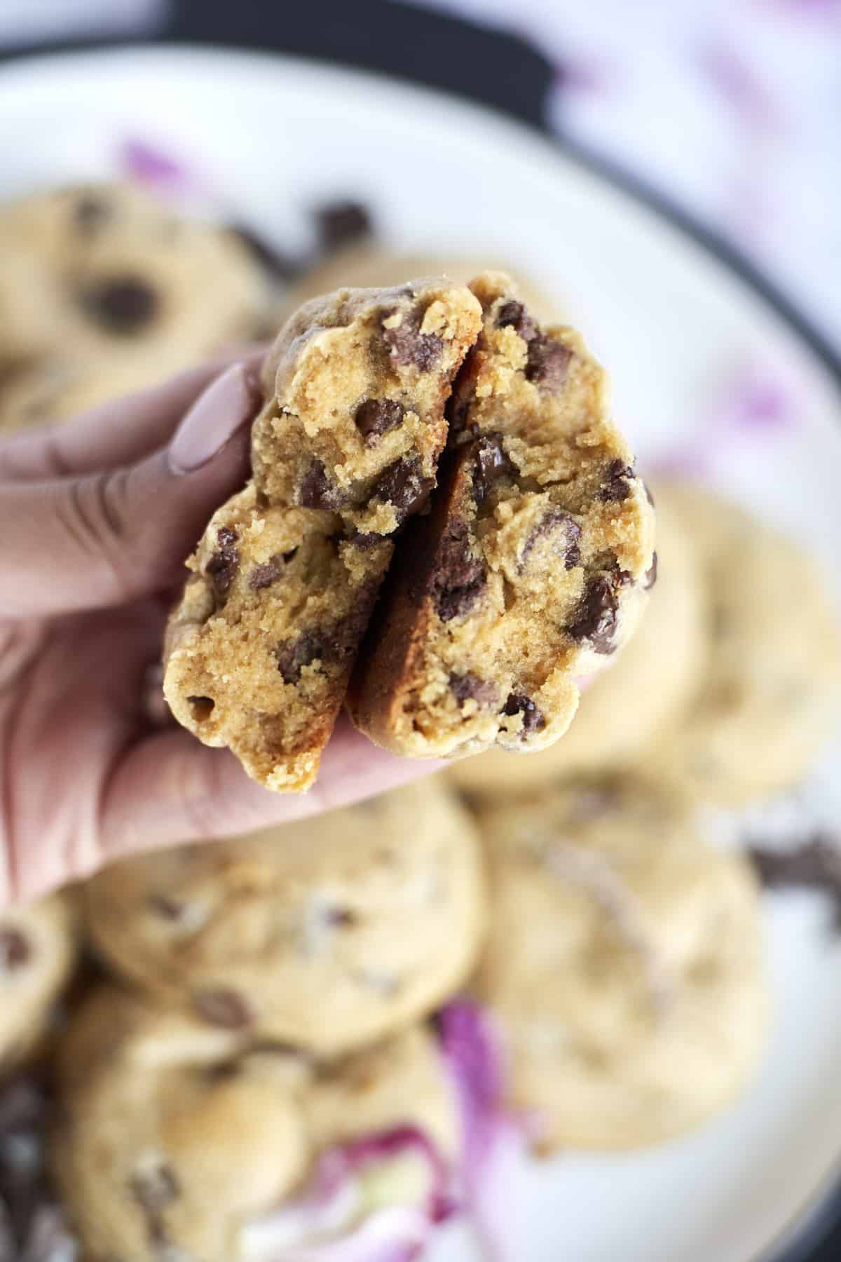 a hand holding two halves of a peanut butter chocolate chunk cookies showing the center