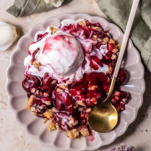 a plate with a serving of cherry crisp topped with ice cream with a spoon on the side