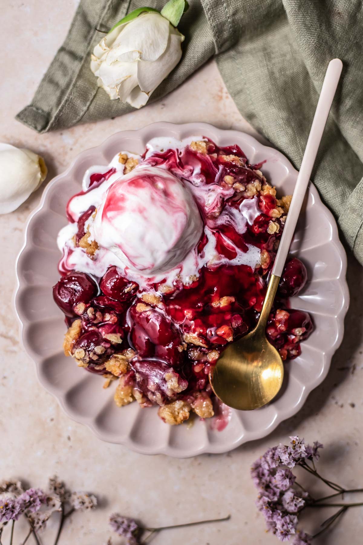a plate with a serving of cherry crisp topped with ice cream with a spoon