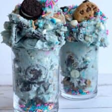 Two jars of edible cookie monster cookie dough topped with Oreos and chocolate chip cookies.