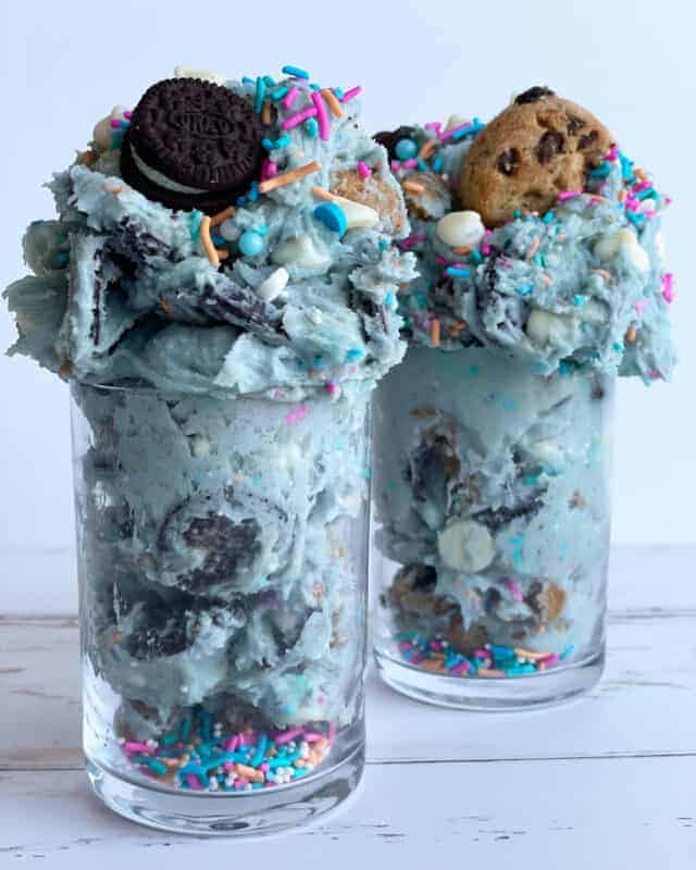 Two jars of edible cookie monster cookie dough topped with Oreos and chocolate chip cookies.