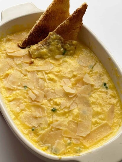 A casserole dish of baked scrambled eggs with two pieces of toasted bread sticking out.