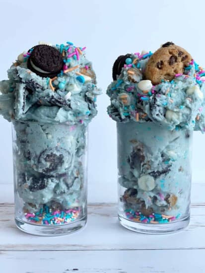 two jars of edible cookie monster cookie dough topped with Oreos and chocolate chip cookies