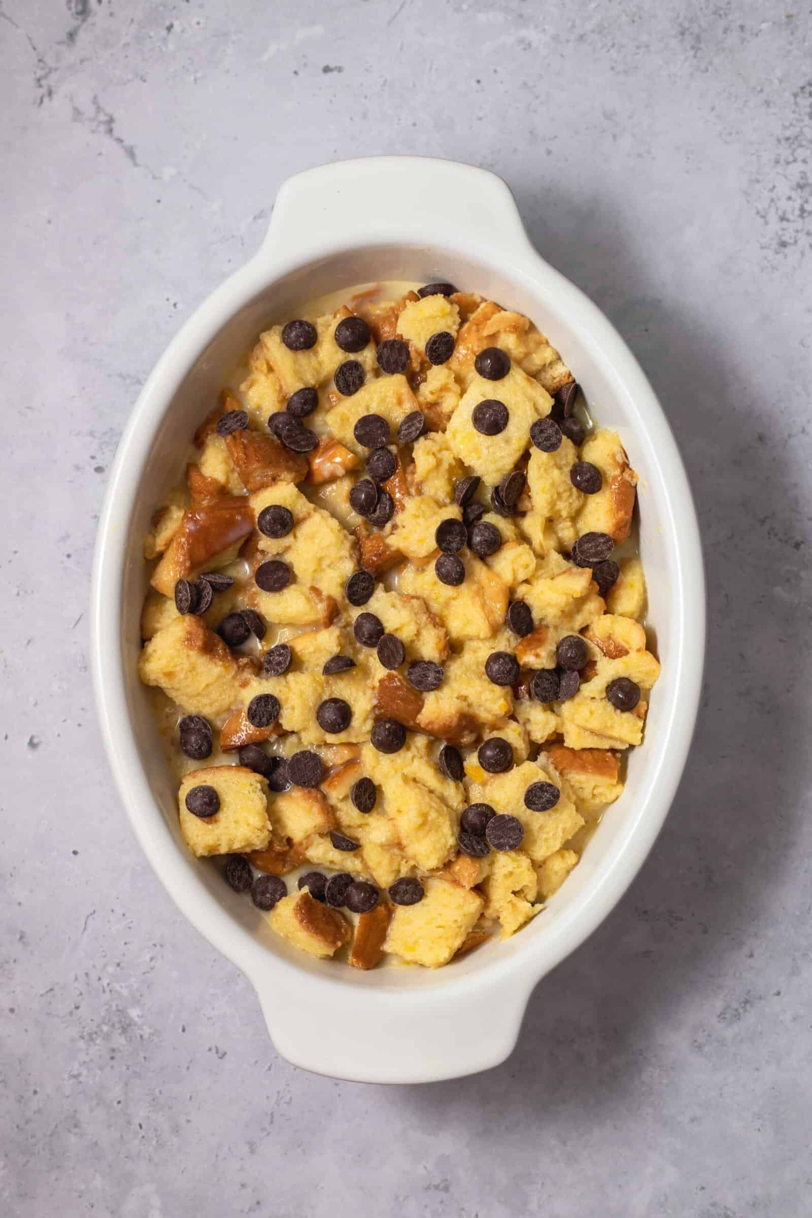 unbaked bread pudding in an oval dish topped with chocolate chips