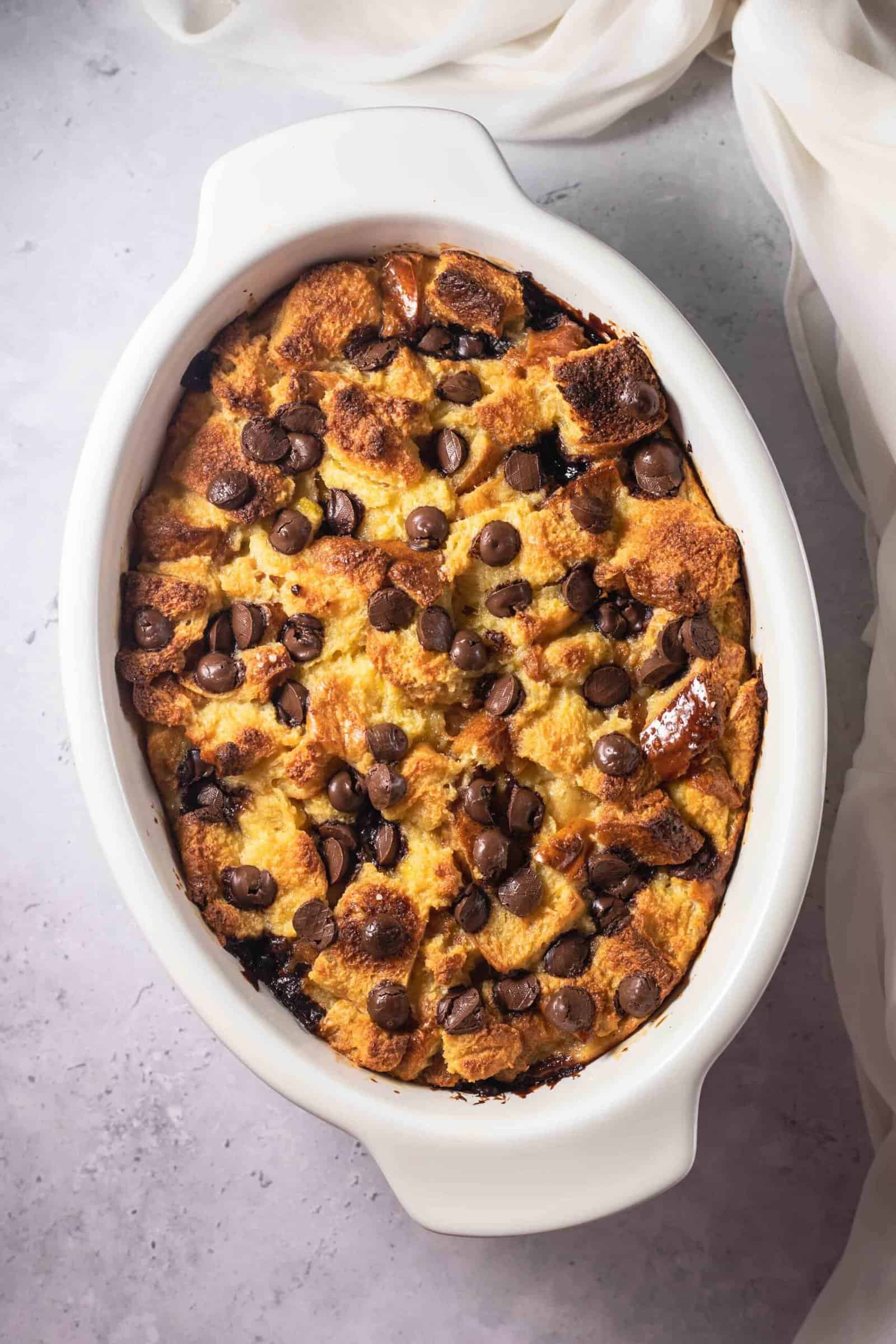 an oval dish full of baked tres leches bread pudding topped with chocolate chips