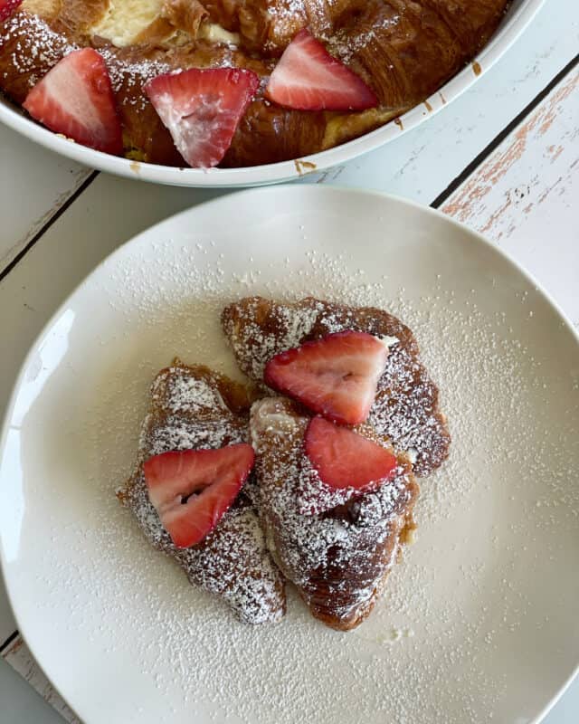 overhead image of a plate of strawberry cheesecake french toast croissants next to a baking dish of french toast