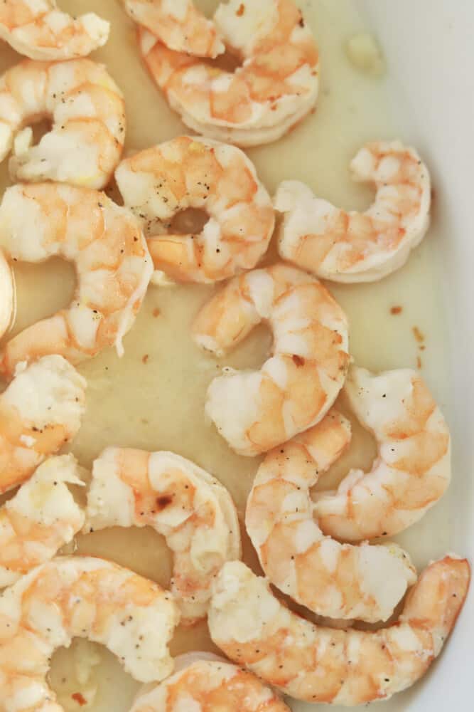 close up image of baked shrimp with garlic and butter in a white baking dish